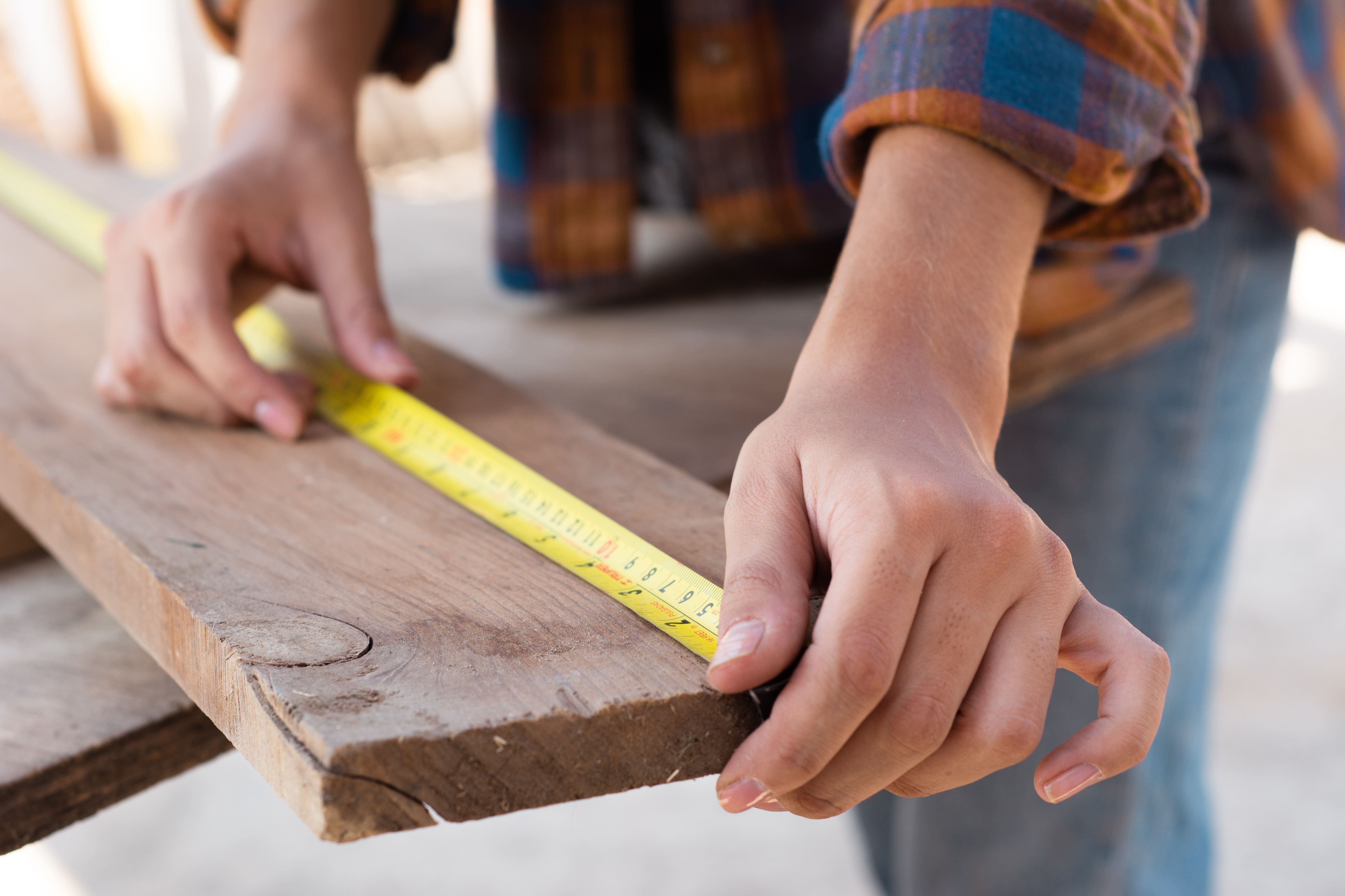 Hands measuring a deck board with a tape measure, illustrating planning and accurate material estimates.