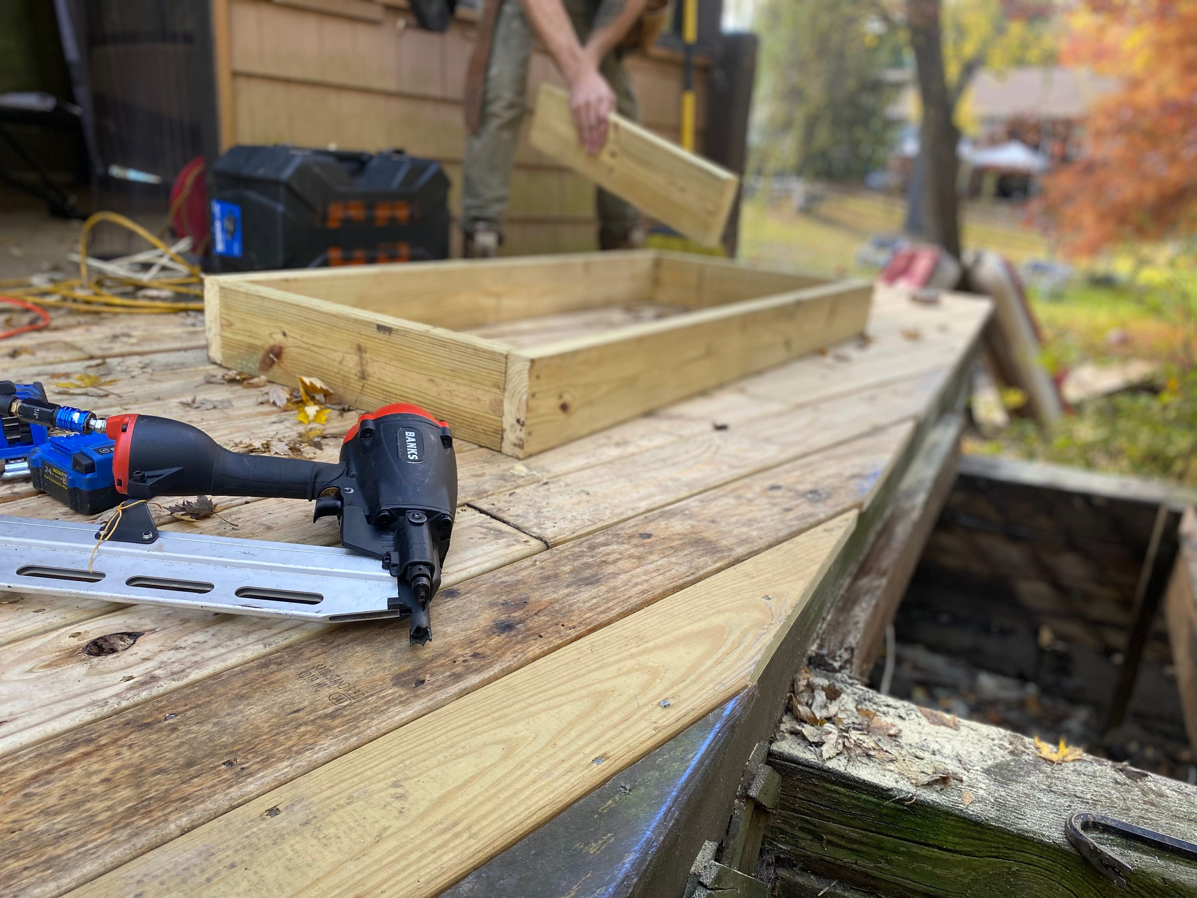 Close-up of deck construction with a nail gun and wood framing, illustrating installation labor and project costs.
