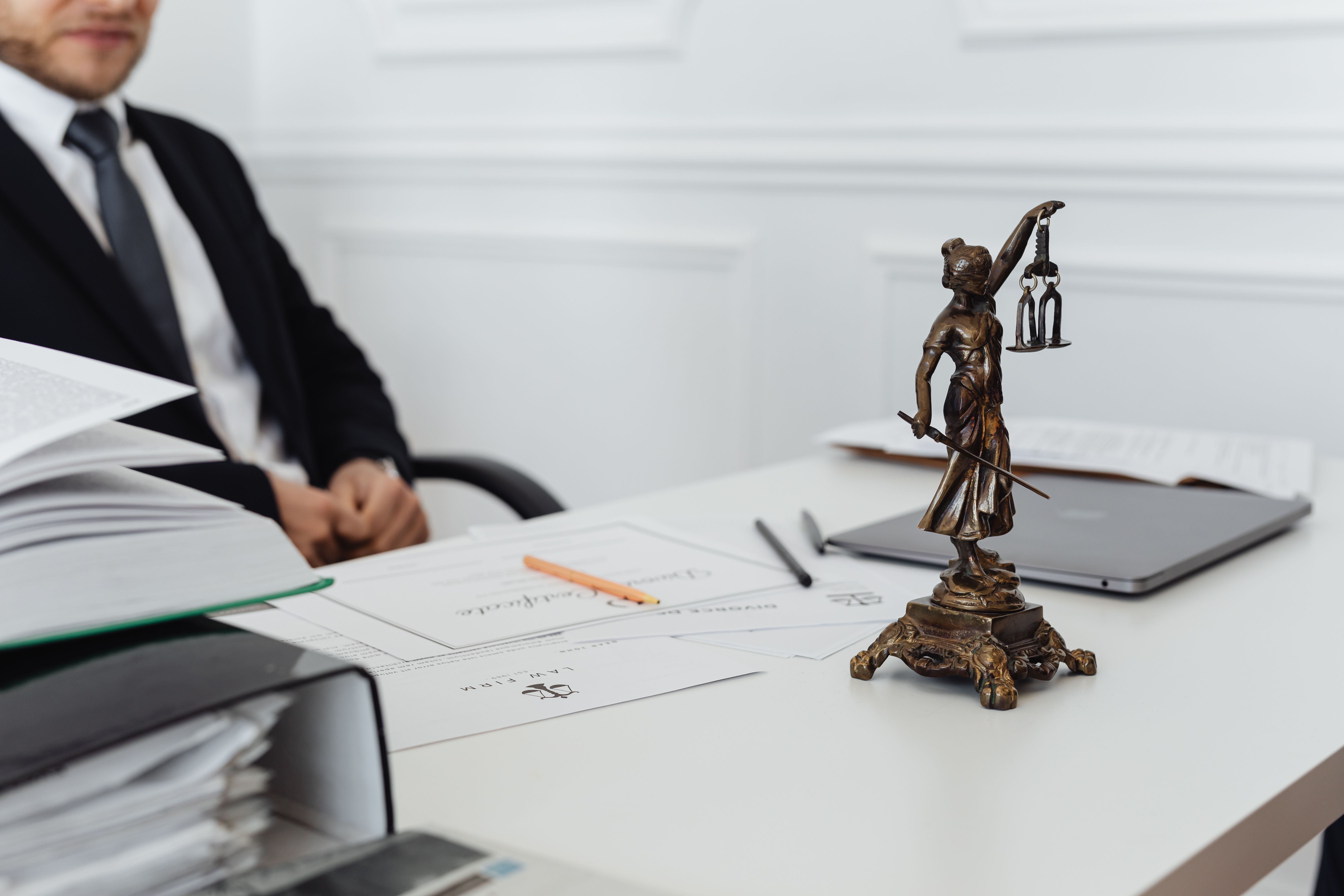 Legal professional workspace with a Lady Justice statue, documents, and laptop, illustrating legal research and accountability.