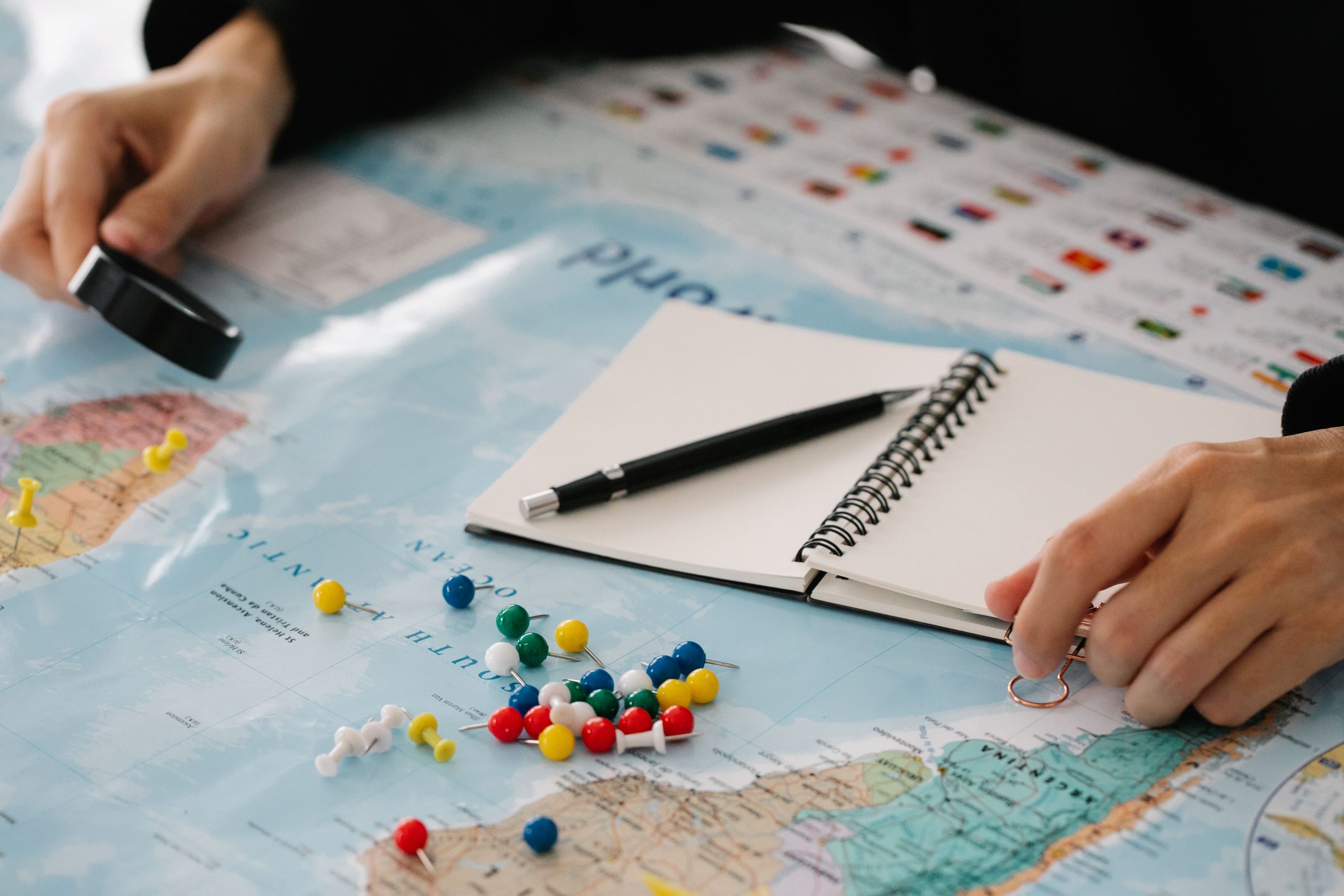 luxury-travel-itinerary-planning Hands planning a bespoke luxury getaway with a map, notebook, and travel pins.