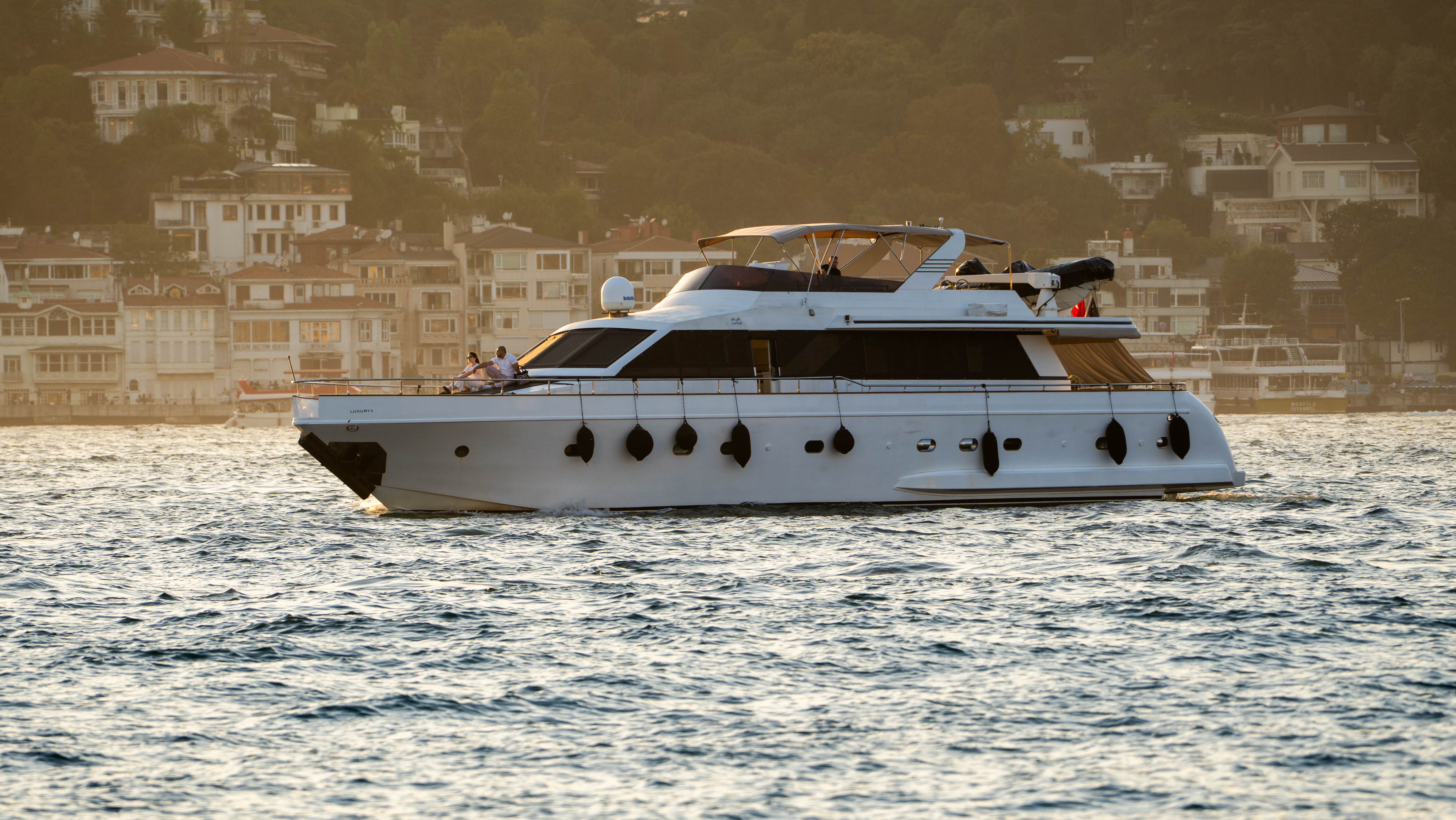 Luxury yacht cruising along a picturesque coastal town at sunset.