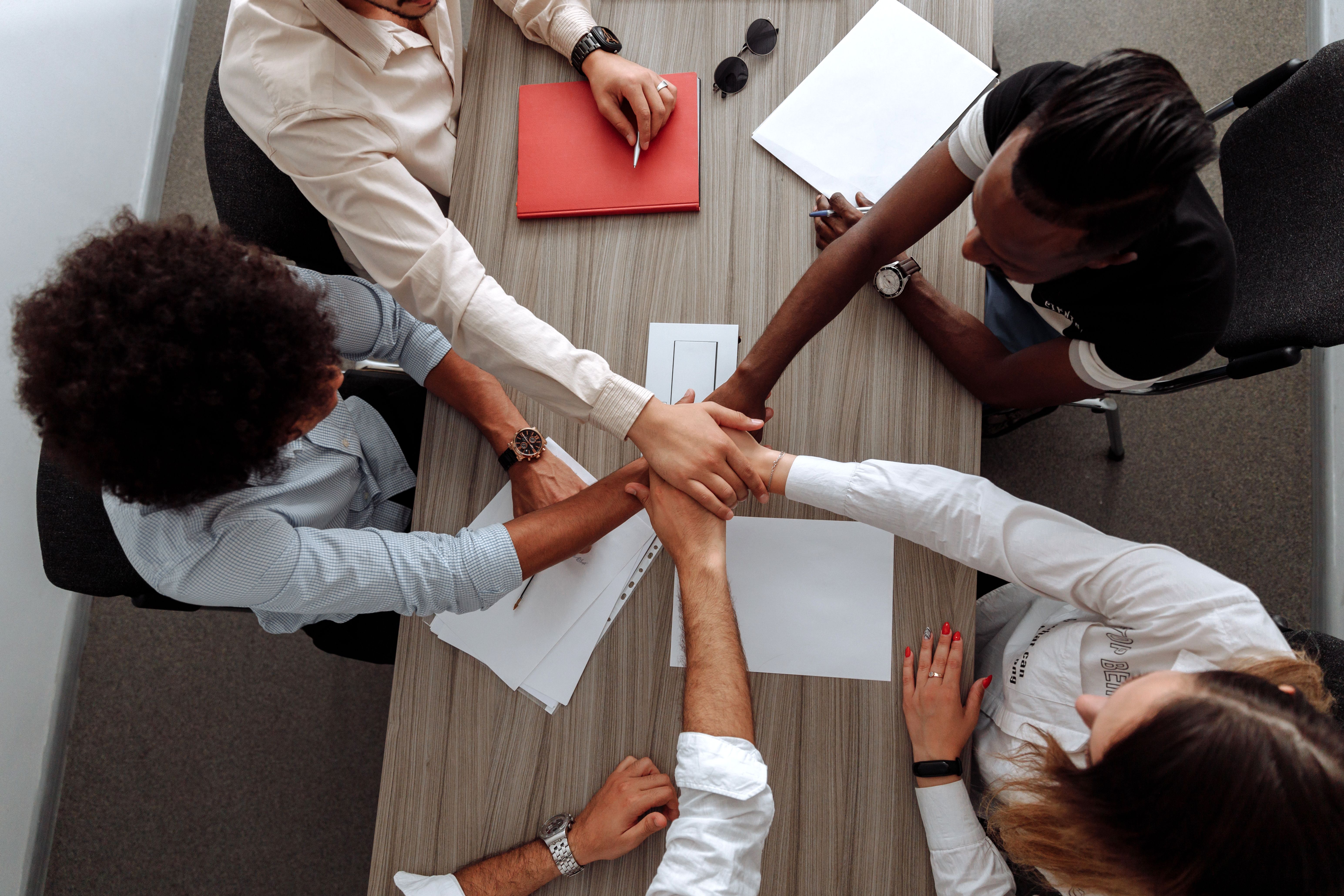 A diverse team placing their hands together to represent unity, shared ownership, and collective accountability.